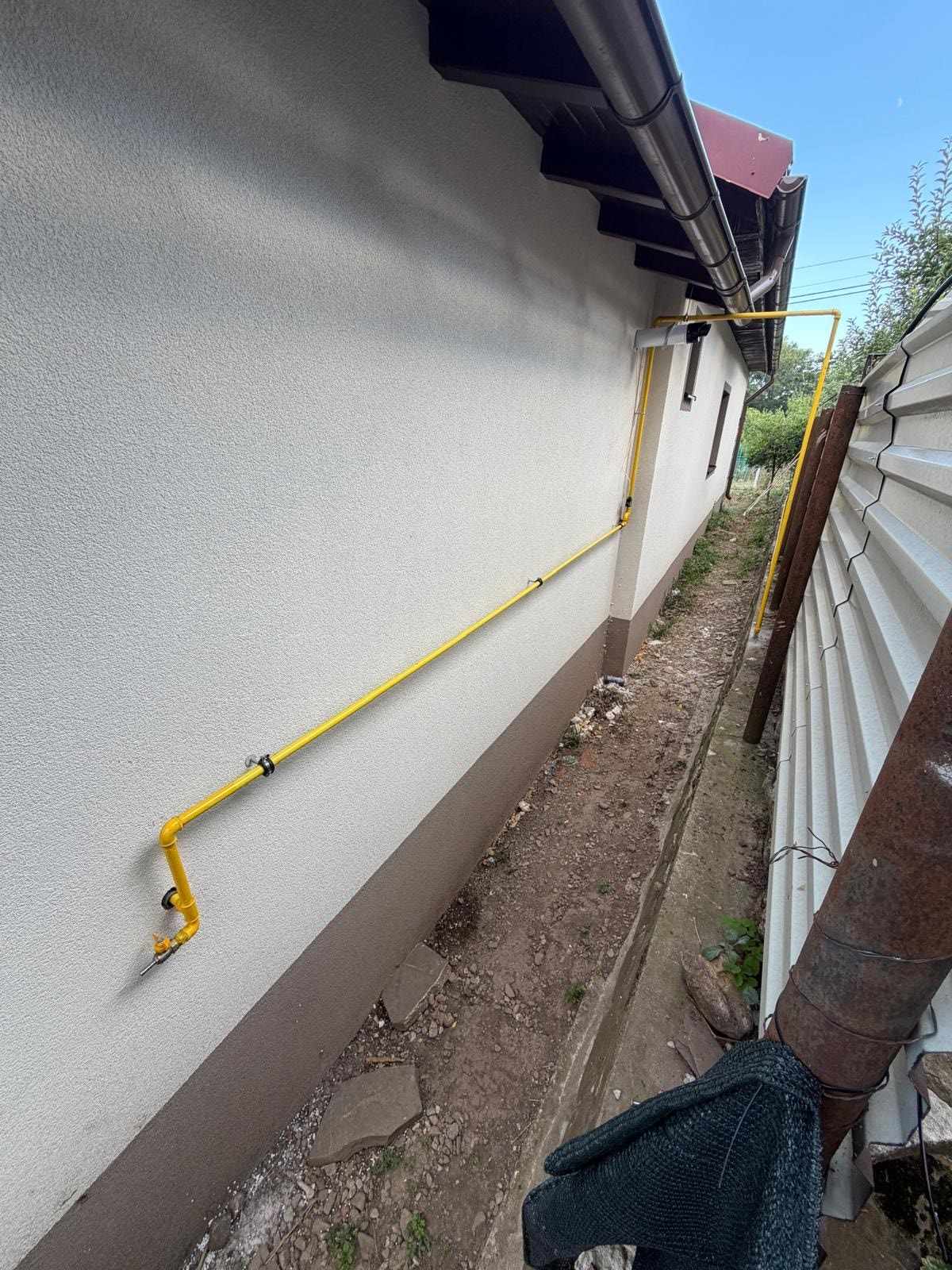 Conductă de gaz vopsită în galben, montată pe fațada unei case, cu robinet de închidere la capătul de jos