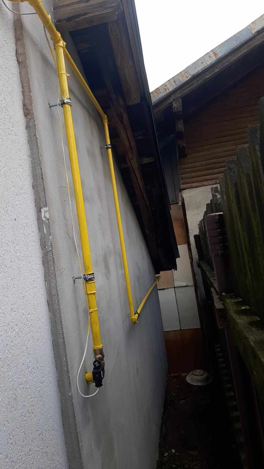 Două conducte de gaz galbene fixate cu brățări pe peretele unei case, sub streașină
