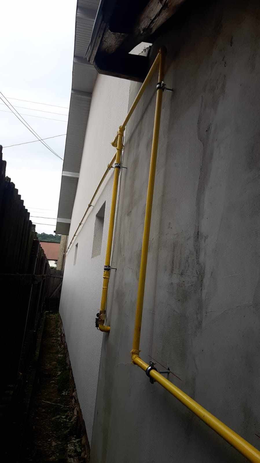 Conducte de gaz galbene pe fațada unei case, cu trasee verticale și orizontale sub streașină