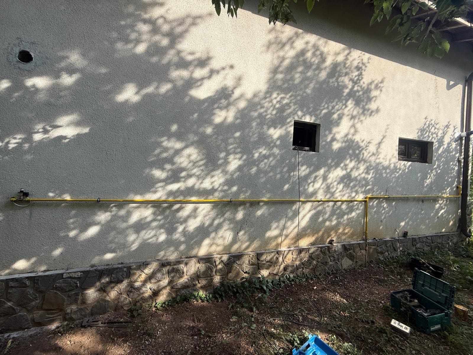 Conductă de gaz galbenă montată orizontal pe peretele exterior al unei case, cu trusa de scule pe iarbă